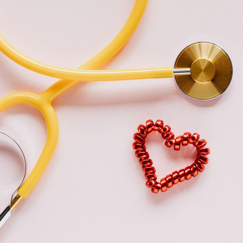 Top view of yellow stethoscope made of plastic and metal material near small handmade heart of spiral hair tie on pale pink b