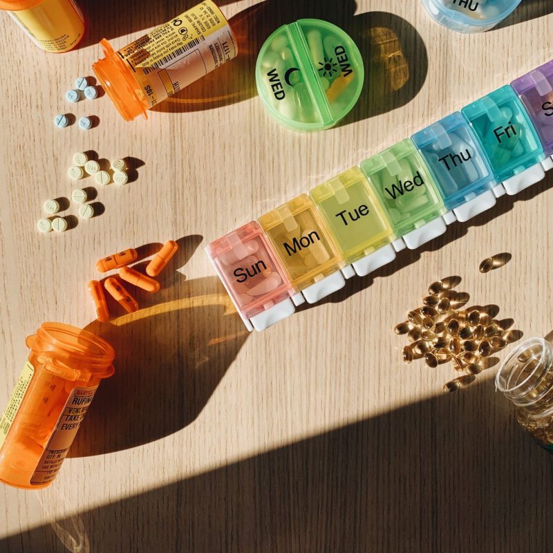 Colorful pill organizer with medication bottles and tablets on a wooden surface. — How About The Counter Hair Discount Therap