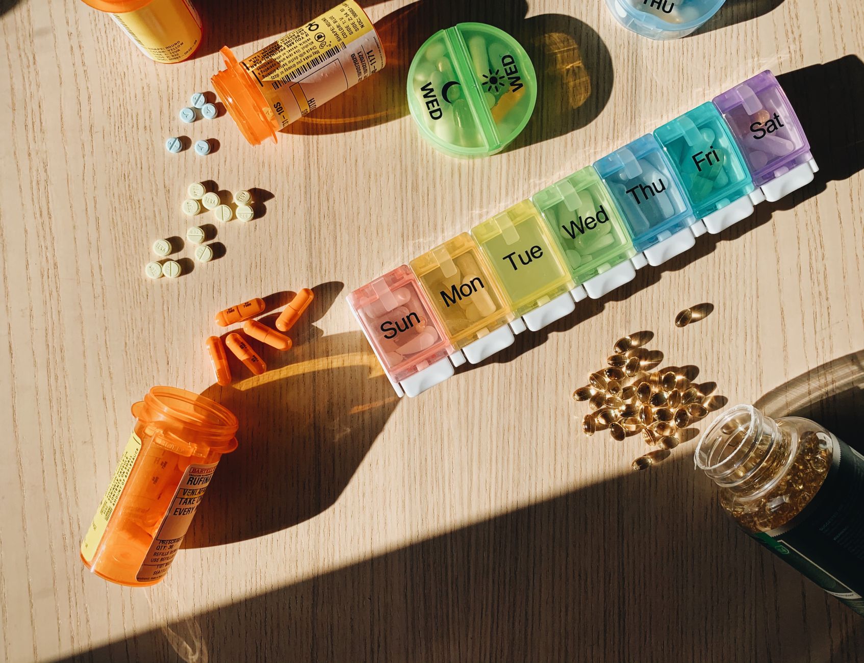 Colorful pill organizer with medication bottles and tablets on a wooden surface. — How About The Counter Hair Discount Therap