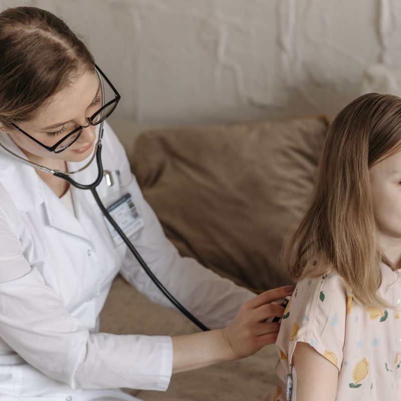 A doctor with a stethoscope examining a smiling girl during a medical check-up at home. — Uncomplicated Meditation Ways